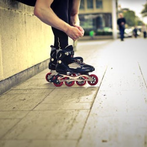 Focused skater adjusting roller blades in a dynamic urban city park setting.