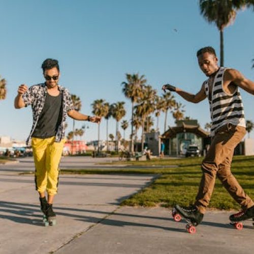 Two young men enjoying roller skating outdoors in a sunny park setting, showcasing skill and fun.